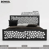 A promotional image of the "ARISTORA Metal Bed" by Bongo. The modern bed frame is made of black metal and features a distinctive decorative design. Both the tall, rectangular headboard and the matching lower footboard have a laser-cut pattern of organic, leaf-like or pebble shapes. The bed is made with dark brown and grey bedding and is set against a plain, light grey background.