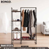 An industrial-style open garment rack from BONGO, featuring a black metal frame and dark wood-grain shelves. The unit has a wide section with a hanging rod on the right and a narrow four-tier shelving tower on the left. The rack is shown in a room setting, fully stocked with winter jackets, ski boots, and goggles.