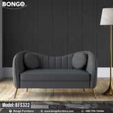 An elegant, Art Deco-style loveseat from BONGO, upholstered in a dark gray fabric and supported by splayed, gold-colored metal legs. The loveseat features a distinctive curved backrest with vertical channel tufting and is accessorized with two matching round pillows. It is shown in a room with a dark gray paneled wall.