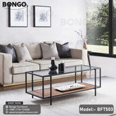 A modern coffee table with a clear glass top, black steel frame, and a wooden shelf underneath. The table is placed in a living room setting with a sofa and cushions in the background.