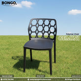 Product photo of the "Gemini Polymer Chair" by BONGO. The black chair features a distinctive backrest with a hexagonal cutout pattern and is displayed outdoors on a green lawn.