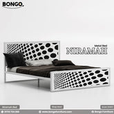 A promotional image of the "NIRAMAH Metal Bed" by Bongo, presented in a high-contrast black and white graphic design. The modern metal bed frame is finished in solid white. The tall, rectangular headboard and matching lower footboard feature a bold pattern of black circles on a white background. The circles gradually increase in size from one side to the other, creating a dynamic gradient or optical illusion effect. The bed is styled with dark grey and brown bedding.