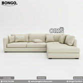 A promotional image of the 'Sofa ORIN', a large, L-shaped sectional sofa upholstered in a light cream fabric. The modern, low-profile design features slim track arms and a right-facing chaise lounge. The sofa is topped with an abundance of assorted plush pillows for a comfortable, relaxed look.