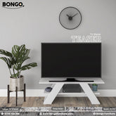 A promotional image of the "TEASER TV Stand" by Bongo, showcased in a modern living room setting. The TV stand is solid white and features a distinctive design with two wide, angled, A-frame style legs and a lower shelf. A large flat-screen television sits on top of the stand. To the left is a large potted plant in a grey pot on a dark wood stand, and on the light grey wall above is a black, minimalist, sunburst-style clock.