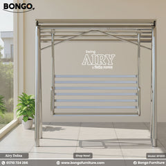 An advertisement for the "Airy" two-seater swing from Bongo Furniture (Model: BFS601). The stainless steel swing is shown in a clean, modern setting on a tiled balcony or patio. To the left is a large window and a lush potted plant. The image features the Bongo Furniture logo and contact information at the bottom.