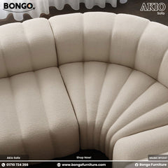 An L-shaped Akio sofa upholstered in beige fabric, featuring a plush design with deep seat cushions and a low-profile structure.