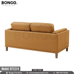 A modern two-seater loveseat upholstered in a smooth, tan-colored leather. The sofa's distinctive features include wide arms with vertical channel tufting on the exterior and tapered, light-colored legs. It is staged with two throw pillows and is pictured in a living room on a dark blue patterned rug.
