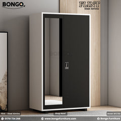 A black steel almirah with a mirror door, positioned against a wall with a painting to the left, on a wooden floor.