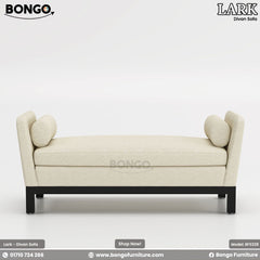 A promotional image of the 'LARK Divan Sofa', a modern, backless settee. The piece is upholstered in a cream-colored fabric and features high, flared arms with matching cylindrical bolster pillows. It is supported by a simple, recessed black frame and legs.