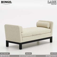 A promotional image of the 'LARK Divan Sofa', a modern, backless settee. The piece is upholstered in a cream-colored fabric and features high, flared arms with matching cylindrical bolster pillows. It is supported by a simple, recessed black frame and legs.