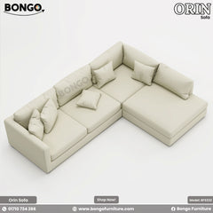 A high-angle view of a large, L-shaped sectional sofa upholstered in a light cream fabric. The modern, low-profile sofa features slim track arms and a right-facing chaise lounge. The back is styled with an abundance of matching plush pillows, creating a relaxed and comfortable appearance.