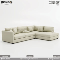 A promotional image of the 'Sofa ORIN', a large, L-shaped sectional sofa upholstered in a light cream fabric. The modern, low-profile design features slim track arms and a right-facing chaise lounge. The sofa is topped with an abundance of assorted plush pillows for a comfortable, relaxed look.

