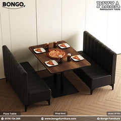 A modern restaurant booth setup, including a rectangular table and two high-backed, facing benches. The benches are upholstered in a dark gray fabric with vertical channel tufting. The table has a dark Water Resistant Strong Laminated Board top and a black pedestal base. The scene is set for a meal, with a large pizza and drinks arranged on the table.