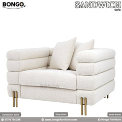 A modern loveseat upholstered in a textured, off-white boucle fabric, viewed from a three-quarters rear angle. The sofa's design is characterized by three large, horizontal channel-tufted sections that wrap around its low back and arms. It is supported by slim, gold-finished metal legs and is shown with two matching triangular throw pillows.