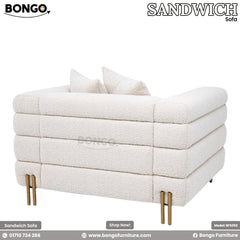 A modern loveseat upholstered in a textured, off-white boucle fabric, viewed from a three-quarters rear angle. The sofa's design is characterized by three large, horizontal channel-tufted sections that wrap around its low back and arms. It is supported by slim, gold-finished metal legs and is shown with two matching triangular throw pillows.