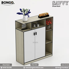 A product photo of a modern storage cabinet or console. The cabinet has a Albino color Water Resistant Strong Laminated Board frame, two central white doors with black trim and handles, and a column of three open shelves on the right. A long, open shelf runs across the top of the unit. The shelves are styled with decorative items, including a vase of purple flowers, a pair of sneakers, a wooden block calendar, and another small vase with red flowers. The brand name "BONGO" is visible on the unit.