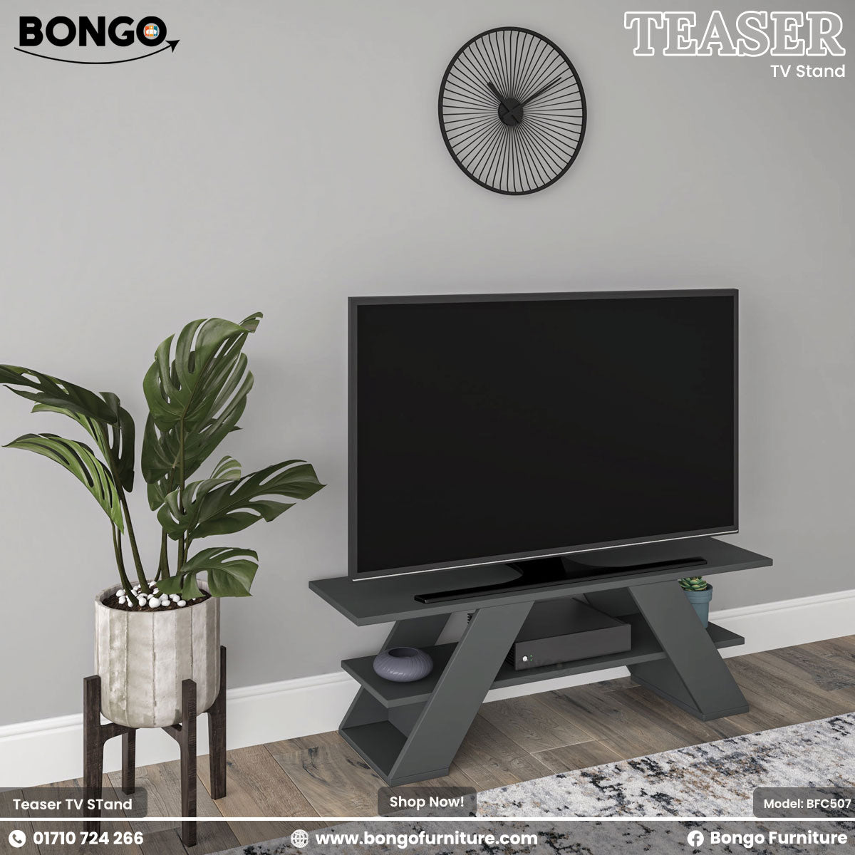 A promotional image of the "TEASER TV Stand" by Bongo, presented in a dark charcoal grey finish. The modern, geometric stand features two wide, angled A-frame style legs and a lower shelf. A large flat-screen television rests on top of the stand. The scene is set against a light grey wall, with a large, leafy potted plant on a stand to the left and a black, minimalist, sunburst-style clock hanging on the wall above. A patterned rug is visible on the floor.