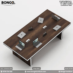 A conference table with a Water Resistant Strong Laminated Board brown tabletop and metal legs, labeled 'VISTA - Conference Table' with a laptop and notepad on top, against a white background.